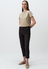 Beżowa bawełniana koszulka z krótkim rękawem, w połączeniu z czarnymi spodniami typu tapered i beżowymi mokasynami. Prosty, codzienny design z minimalnymi detalami.