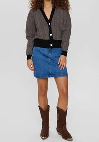 Černý a krémový cardigan ve vzoru rybí kost s hlubokým výstřihem do V a velkými knoflíky, kombinovaný s modrou džínovou mini sukní a hnědými botami v západním stylu.