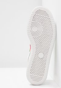 Semelle d'une basket blanche avec des motifs de traction circulaires et hexagonaux, montrant des zones antidérapantes texturées et une partie supérieure colorée.