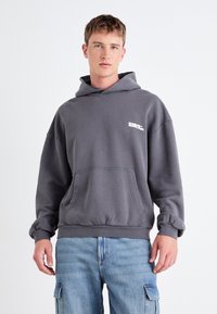 Hoodie gris en mélange de coton, avec une poche avant, des manches à bords-côtes et un logo blanc sur la poitrine. Design décontracté et ajustement relaxed.