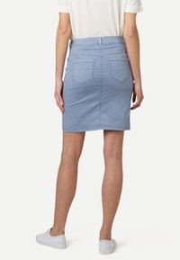 Falda de mezclilla azul claro con un diseño ajustado, de longitud hasta medio muslo, con dos bolsillos traseros y pasadores para cinturón. Combinada con una camiseta blanca y zapatos.