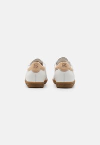 Chaussures en cuir blanc avec des accents beige, de forme ronde, texture lisse et semelle en caoutchouc marron. Présente un logo "paul green" en relief sur le talon.