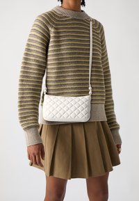 Borsa a tracolla bianca trapuntata con finitura liscia, dotata di tracolla removibile e di un logo discreto nella parte frontale.