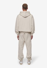 Cremefarvet hættetrøje og matchende joggers lavet af blødt stof. Har en hætte, ribbede manchetter og tapered ankler. Hvide sneakers med beige såler.