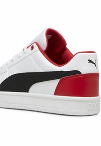 Vit sneaker med svart sidostreck, röd häl och innersula, vita snören och Puma-logotyp på hälen och sulan.