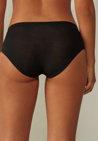 Zwarte katoenen slip met een gladde textuur, een medium hoge taille en naadloze randen. De achterkant heeft een afgeronde snit voor extra comfort.