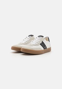 Weiß-graue Sneaker mit einer Wildleder-Textur, ausgestattet mit einem schwarzen Akzentstreifen, flachen weißen Schnürsenkeln und einer Sohle aus Gummi.
