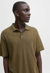 Olivgrön polo t-shirt med en strukturerad geometrisk mönster, korta ärmar och en klassisk krage med en tvåknappars placket.