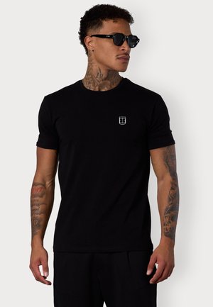 Black cotton t-shirt with a crew neck, short sleeves, and a small white logo on the left chest. Smooth texture, fitted design.