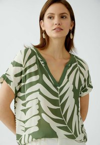 Korte mouwen, v-hals blouse in het groen met een wit bladerenpatroon, gemaakt van een lichte stof. Heeft een ontspannen pasvorm en een soepele textuur.