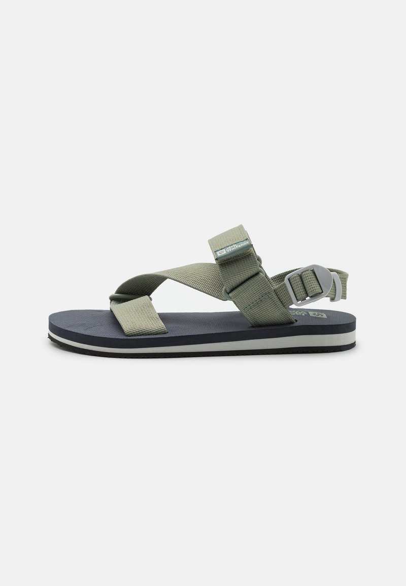 Green and gray sandal with cross-strap design, a textured footbed, and a two-tone sole. Adjustable buckle for secure fit.