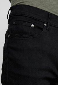 Svart denimjeans med en mjuk textur, utrustade med silverdetaljer, en klassisk femficksdesign och en medelhög midja.