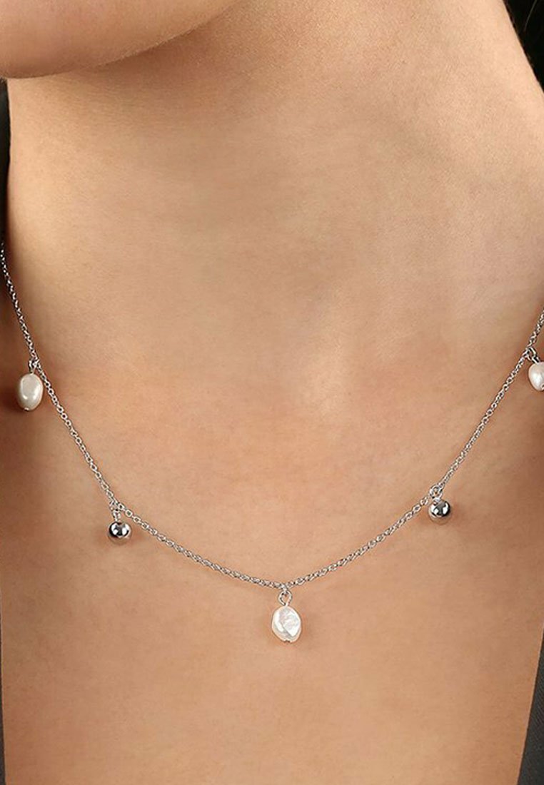 Collana in argento con tre pendenti: una perla bianca, una pallina in argento e un ciondolo ovale con superficie texture.