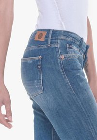 Jeans de mezclilla azul oscuro con un corte ajustado, que presentan una etiqueta de parche de cuero en la cintura, un sutil desgaste y un clásico diseño de cinco bolsillos.