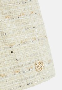 Světle béžová tkanina s metalickými akcenty, s texturovaným povrchem. Obsahuje detail loga ve zlatém odstínu na spodní části.
