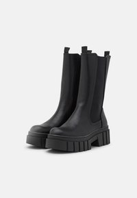 Black ankle boots made of smooth leather with elastic side panels, chunky platform soles, and two pull tabs for easy wear.