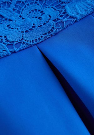 Blauer Stoff mit filigranen Spitze-Details an der Oberseite und einer ordentlich genähten vertikalen Naht. Die Textur ist glatt mit einem matten Finish.