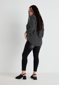 Black and white vertically striped shirt with rolled sleeves, paired with black skinny jeans and black heeled sandals. Smooth textures, casual style.