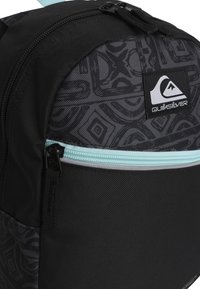 Mochila negra de Quiksilver con tela estampada, cremallera azul claro y parche del logo. Presenta una parte superior redondeada y una superficie texturizada.