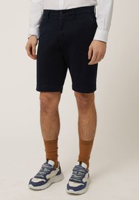Marineblauwe shorts van een katoenmix, met een vlakke voorkant, zijzakken en omgeslagen zoom, gecombineerd met bruine enkelsokken en sneakers.