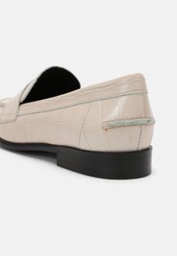 Mocassino in pelle beige con stampa cocodrillo, suola piatta nera e dettagli in cucitura azzurro chiaro sulla parte superiore e sul tallone.