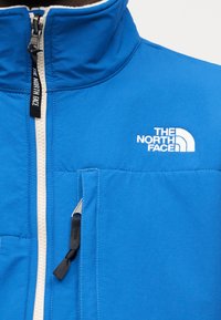 Μπλε μονωμένο μπουφάν με ψηλό γιακά, φερμουάρ μπροστά, λευκό λογότυπο στο στήθος και μαύρο τράβηγμα φερμουάρ με ταμπελάκι. Διαθέτει τσέπη στο στήθος.