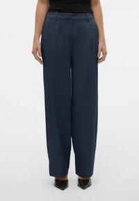 Wijd beenbroek van donkerblauwe stof, met voorplooien en een gladde textuur. Inclusief riemlussen en een lichte tapering bij de zoom.