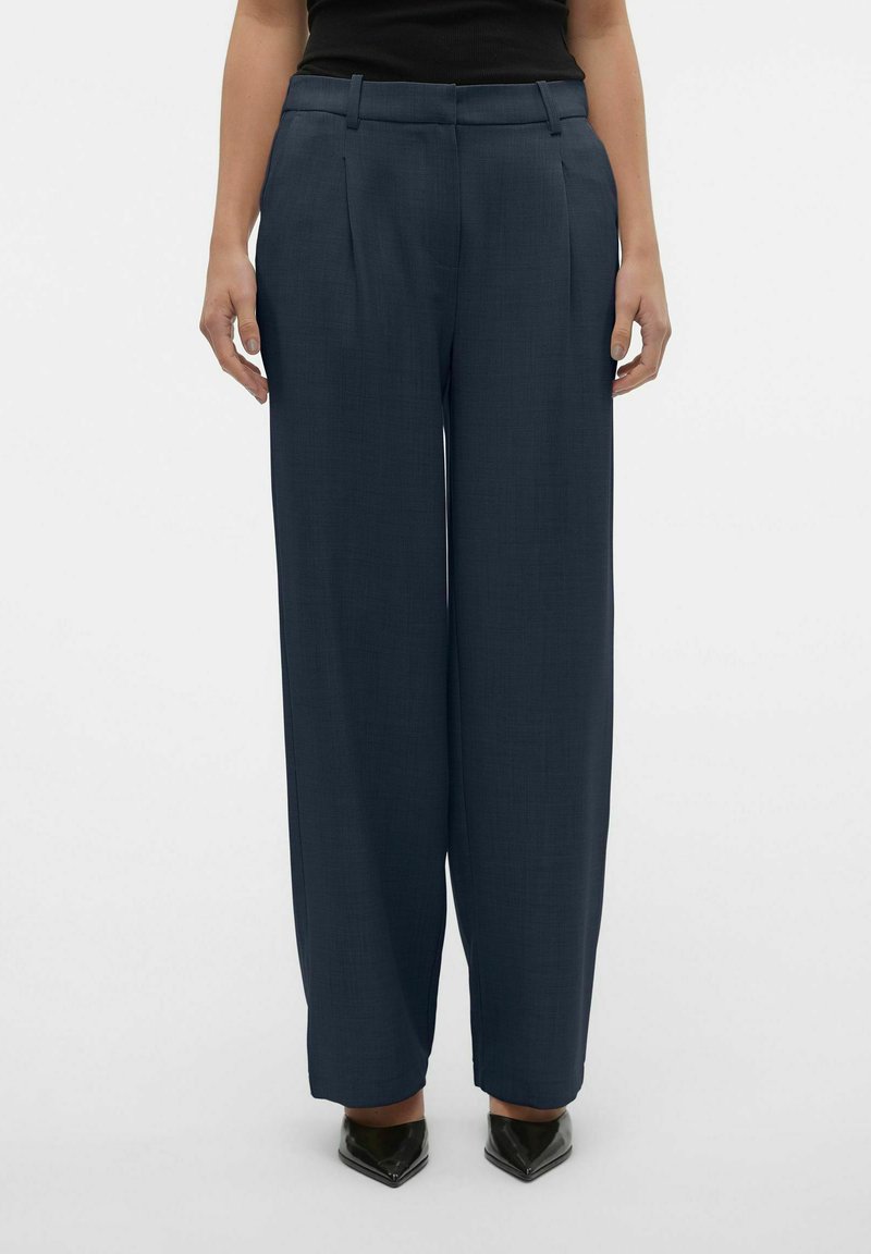 Wijd beenbroek van donkerblauwe stof, met voorplooien en een gladde textuur. Inclusief riemlussen en een lichte tapering bij de zoom.