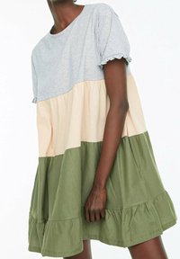 Robe à blocs de couleur avec un haut gris, un milieu beige et un bas olive. Silhouette évasée avec des bords de manches volants et un ourlet en dentelle.