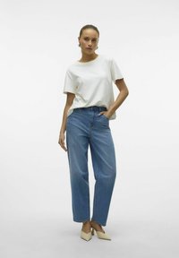 Camiseta blanca de manga corta combinada con jeans azul de cintura alta. La modelo lleva tacones de punta beige. Diseño sencillo, ajuste relajado.
