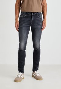 Pánske tmavosivé úzke džínsy z denimu so zosvetleným povrchom, piatimi vreckami a jemným prešívaním. Kombinované so svetlými teniskami.