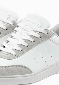Weiße und graue Sneaker mit einem glatten Lederobermaterial und Wildlederakzenten, ausgestattet mit weißen Schnürsenkeln und durchbrochenen Details an den Seiten.