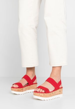 Red wedge sandals with cork platform, white rubber sole, and wide straps crossing the foot. Features a textured cork pattern.