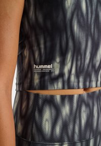 Sporttop i ett vågigt svart och grått mönster. Har en cropped design, stretchigt material och en logotyp på nedre vänstra sidan.