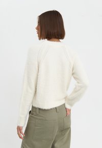 Witte fluffy trui met een ronde hals en geribbelde mouwen, gecombineerd met hooggetailleerde olijfgroene cargobroeken met grote achterzakken.