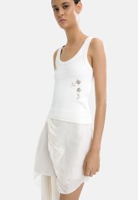 Biały ribbed top z kwiatowymi zdobieniami, w połączeniu z lekką, zwiewną kremową spódnicą. Całość wygląda minimalistycznie i elegancko.