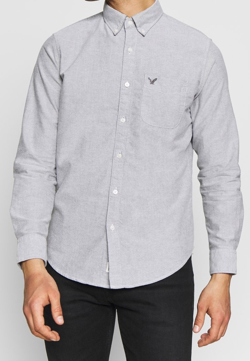 Šedá košile na knoflíky s dlouhými rukávy, náprsní kapsou a malým logem orla. Vyrobena z měkké, strukturované tkaniny s zaobleným lemem.