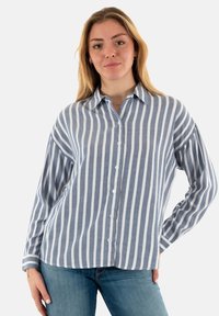 Camisa de botón a rayas azul y blanca con cuello, mangas largas y un corte relajado. Confeccionada en una mezcla de algodón ligero.