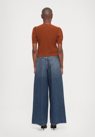 Rust-colored short-sleeve knit sweater with a scalloped hem, paired with wide-leg blue denim jeans featuring standard pockets.