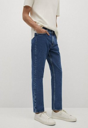 Jeans de mezclilla en un tono azul oscuro, diseño de pierna recta, con bolsillos frontales y costuras sutiles, combinados con zapatillas blancas y una blusa clara.