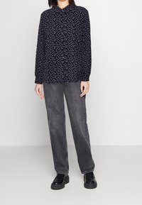 Navy button-up shirt with white polka dots, long sleeves, and a classic collar, paired with gray straight-leg jeans and black platform shoes.