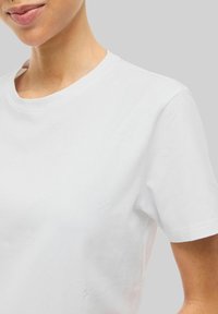 Vit bomullströja med rund hals, korta ärmar och en subtil präglad stjärnvariant. Slät textur och avslappnad passform.