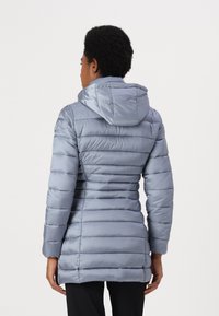Giacca puffa azzurra chiara con cappuccio. Pattern a righe orizzontali, di lunghezza intermedia e texture liscia. Presenta tasche con zip sui lati.