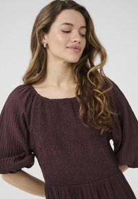 Robe bordeaux avec un décolleté carré, texture froncée et manches bouffantes. Tissu doux qui tombe de la taille. Design simple et élégant.