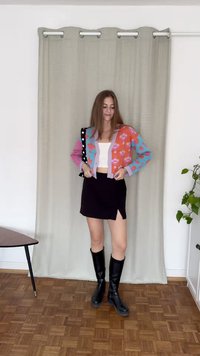 Kleurige cardigan met bloemenpatroon in roze en blauw, gecombineerd met een zwarte minirok met een zijopening, en kniehoge zwarte laarzen.