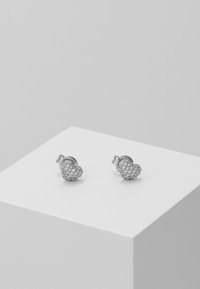 Silverfärgade örhängen i hjärtform prydda med klara rhinstenar. Slät textur med en polerad yta och säker postback.