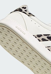 White Adidas sneaker with textured sole, black leopard print on heel and stripes, and embossed Adidas logo on the midsole.