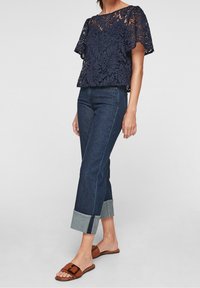 Haut en dentelle navy à manches courtes, associé à un jean en denim noir courts avec un revers en denim plus clair et des sandales à brides marron.