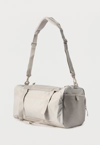 Κυλινδρική τσάντα τύπου duffel σε ανοιχτό γκρι χρώμα με ρυθμιζόμενο λουρί ώμου, δίχτυ στην πλαϊνή τσέπη και διπλές λαβές μεταφοράς σε λευκό φόντο.