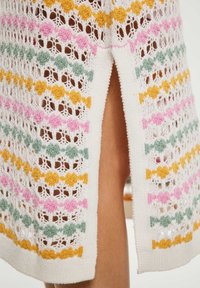 Rochie tricotată cu o bază albă și modele zigzag colorate în roz, portocaliu, verde și galben. Fisura laterală adaugă detaliu.
